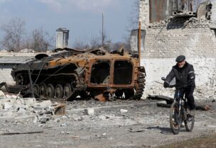 رجل يقود درّاجته الهوائية بجانب آلية مدمرة في أوكرانيا (رويترز)