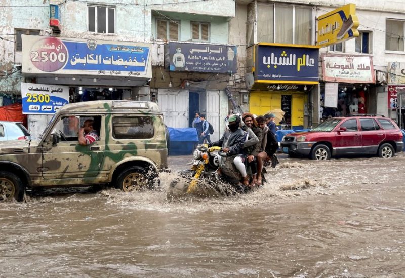 أشخاص يركبون دراجة نارية في شارع غمرته المياه نتيجة هطول أمطار غزيرة بصنعاء