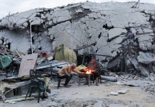فلسطينيون يجلسون بجانب النار بجانب مبنى دمر خلال الهجوم الإسرائيلي. رويترز