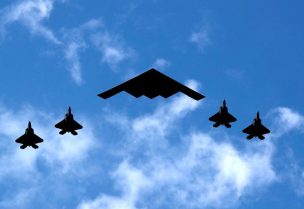قاذفة قنابل شبحية من طراز B-2 سبيريت التابعة للقوات الجوية الأمريكية (C) تحيط بها 4 مقاتلات من طراز F-35 تابعة لمشاة البحرية الأمريكية