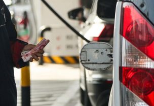 موظف يمسك أوراقا نقدية باليوان الصيني بجانب غطاء مفتوح لخزان وقود سيارة في محطة وقود ببكين يوم 22 مارس آذار 2026. تصوير: مكسيم شيمتوف - رويترز