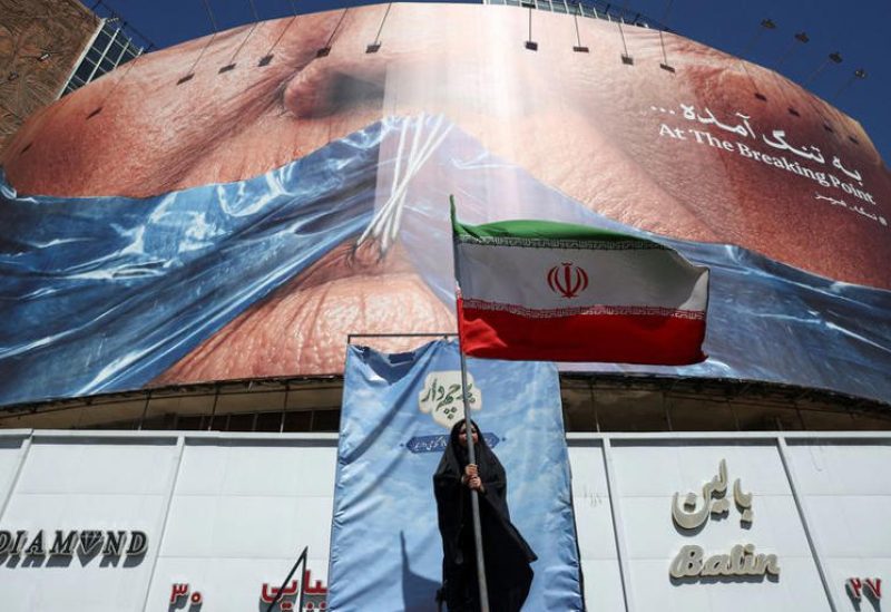 امرأة تحمل العلم الإيراني قرب لوحة إعلانية مناهضة للولايات المتحدة الأمريكية، تُصوّر الرئيس الأمريكي دونالد ترامب ومضيق هرمز، في طهران يوم 25 مايو أيار 2026. صورة من وكالة أنباء غرب آسيا (وانا) حصلت عليها رويترز من طرف ثالث.