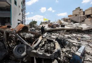 امرأة تحمل علم حزب الله وسط أنقاض مبان مدمرة في دير قانون النهر بقضاء صور في جنوب لبنان