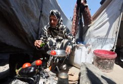 امرأة فلسطينية نازحة تطهو الخضار على نار الحطب خارج خيمتها، في خان يونس، بجنوب قطاع غزة، 21 يوليو 2026. رويترز